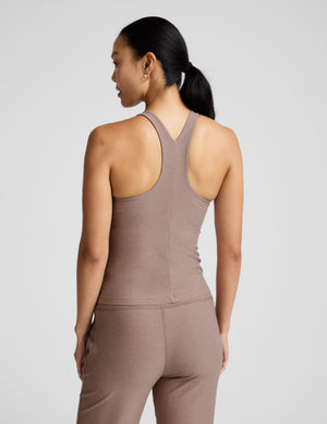 Woman wearing a brown high-neck tank top and pants against a plain background. 