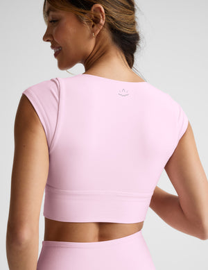 Woman in pink cropped twist tee and leggings on a light gray background. 