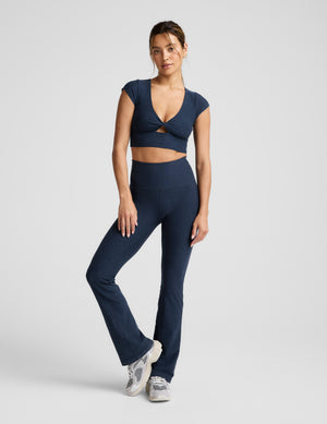 Woman wearing a navy blue cropped twist tee and pants on a light gray background. 