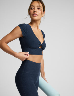 Woman wearing a navy blue cropped twist tee and pants on a light gray background. 