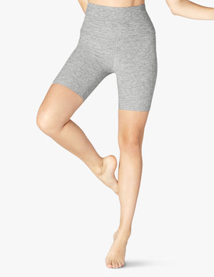 A person wears light gray Spacedye High Waisted Biker Shorts in a mid-thigh length with one leg lifted in a yoga pose.