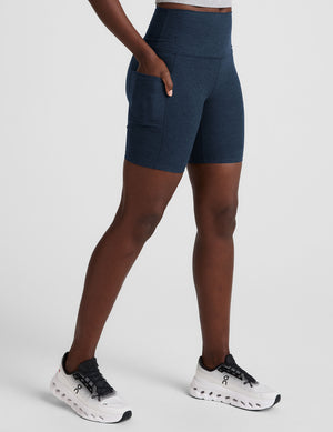 woman wearing navy blue biker shorts with pockets on a plain background. 