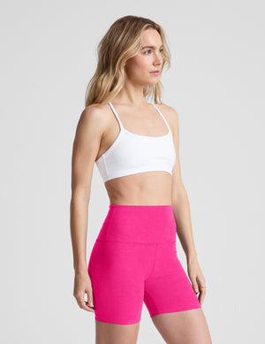 Woman wearing a white sports bra and pink high-waisted shorts on a light gray background. 