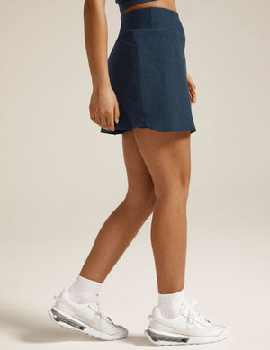 Side profile of woman wearing Navy Spacedye™ Movement Skirt with a wide waistband and curved hem, with white sneakers.