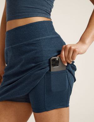 Woman wearing Navy Spacedye Movement Skirt with a matching top, showing a phone in the built-in shorts side pocket.