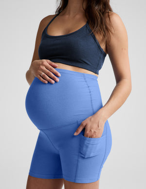 Woman wearing a blue bra and maternity shorts against a plain background. 