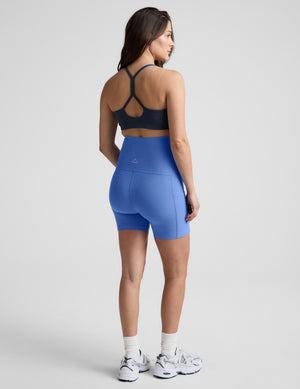 Woman wearing a blue bra and maternity shorts against a plain background. 