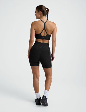 woman wearing a black sports bra and pocket biker shorts shorts on a plain background. 