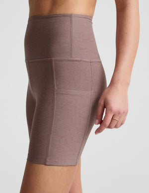 Woman is wearing brown biker shorts with pockets against a plain background. 