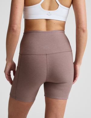 Woman is wearing brown biker shorts with pockets against a plain background. 