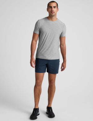 man wearing a grey t-shirt and navy blue shorts on a plain background. 