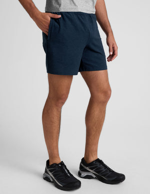 man wearing a grey t-shirt and navy blue shorts on a plain background. 