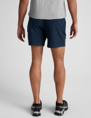 man wearing a grey t-shirt and navy blue shorts on a plain background. 