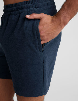 man wearing a grey t-shirt and navy blue shorts on a plain background. 