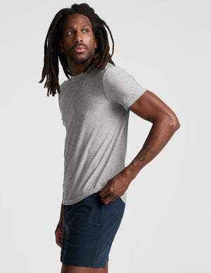man wearing a grey t-shirt and navy blue shorts on a plain background. 