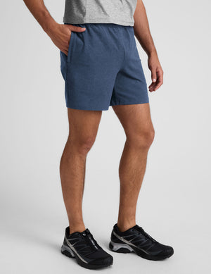 man wearing a grey t-shirt and blue shorts on a plain background. 