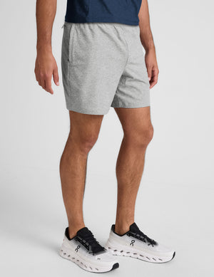 man wearing a navy t-shirt and gray shorts on a plain background. 