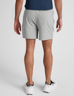 man wearing a navy t-shirt and gray shorts on a plain background. 