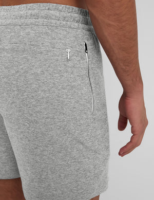 man wearing a navy t-shirt and gray shorts on a plain background. 