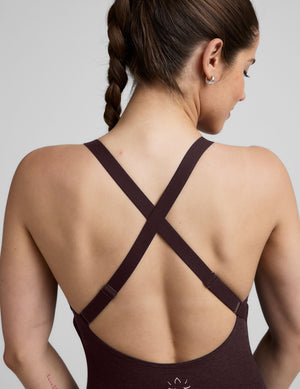 woman wearing a dark brown midi length jumpsuit on a plain background. 