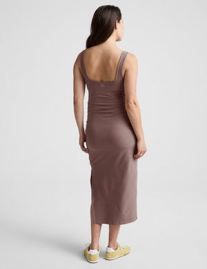 Woman wearing a brown maternity midi length dress against a plain background. 