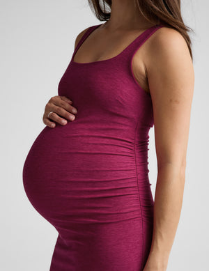 Woman wearing a magenta maternity midi length dress against a plain background. 