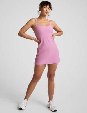 model is wearing a pink mini length dress with slim adjustable straps and built-in shorts with pockets. 