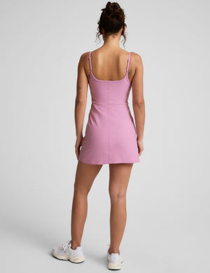 model is wearing a pink mini length dress with slim adjustable straps and built-in shorts with pockets. 
