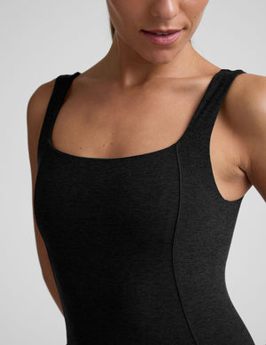 model wearing a black square neck and bootcut jumpsuit on a gray background. 