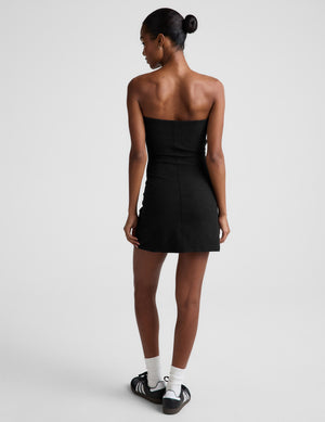 Woman wearing a black strapless mini dress on a plain background. 