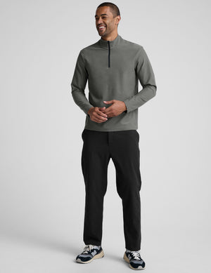 man wearing a gray quarter zip pullover with black pants and a plain background. 