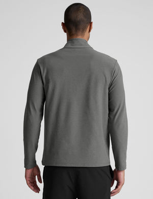 man wearing a gray quarter zip pullover with black pants and a plain background. 