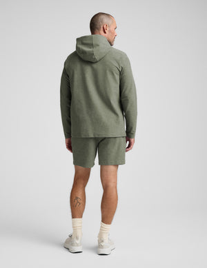 Man wearing a green hoodie and shorts set on a white background. 