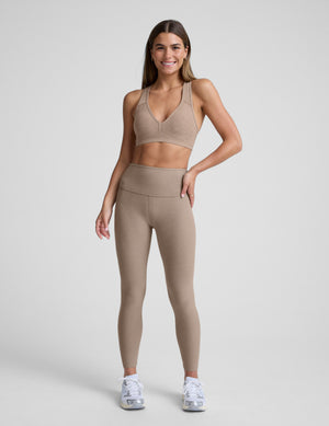 Woman wearing a beige bra with matching leggings against a plain background. 