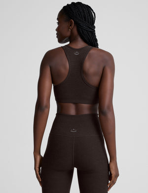 woman wearing a brown v-neck sports bra and pants on a plain background. 