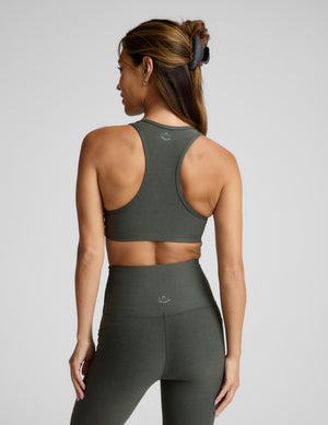 Woman wearing a green sports bra and leggings on a gray background. 