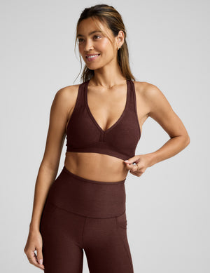 Woman wearing a brown sports bra and leggings against a light gray background. 