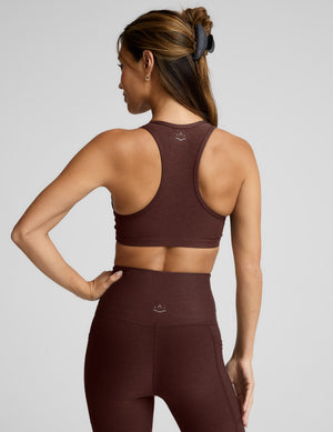 Woman wearing a brown sports bra and leggings against a light gray background. 