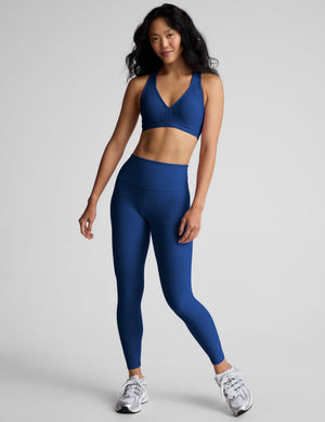 woman wearing a blue sports bra and leggings on a gray background. 