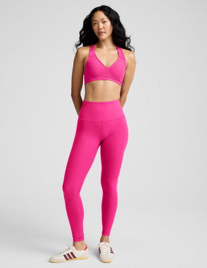 Woman wearing a pink sports bra and leggings on a gray background. 