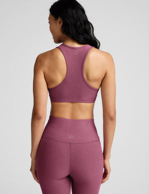 Woman wearing a purple bra and leggings against a plain background. 