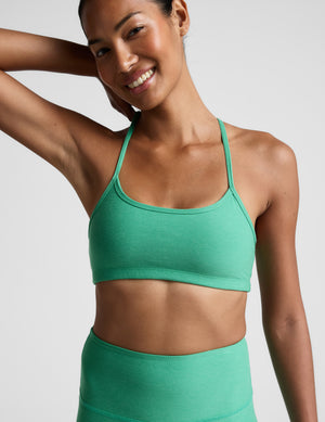 Woman wearing a green sports bra and leggings against a plain background. 