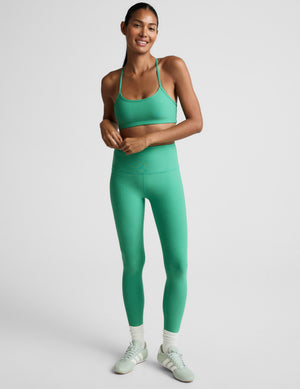 Woman wearing a green sports bra and leggings against a plain background. 