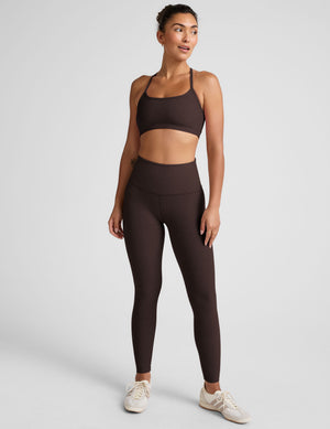 Woman wearing a brown racerback sports bra and leggings on a light gray background. 
