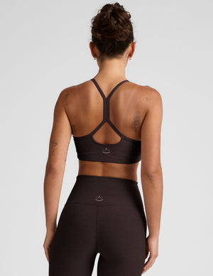 Woman wearing a brown racerback sports bra and leggings on a light gray background. 