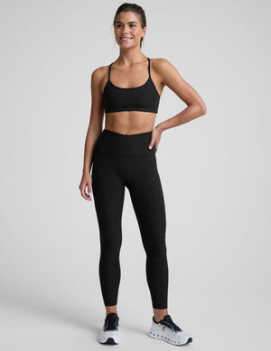 woman wearing a black slim racerback bra and leggings on a plain background. 