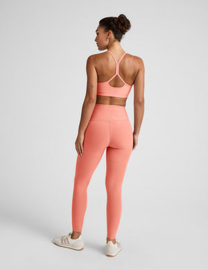 Woman wearing a coral sports bra and leggings set on a light gray background. 