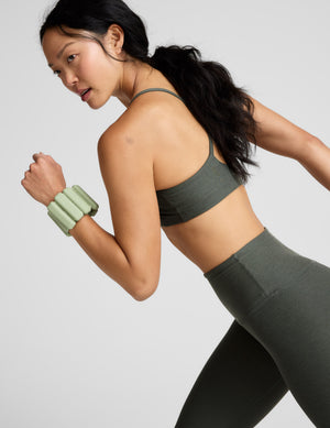 Woman wearing a green sports bra and leggings on a light gray background. 