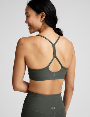 Woman wearing a green sports bra and leggings on a light gray background. 