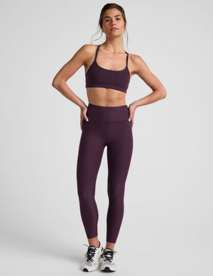 Woman wearing a purple slim racerback bra and leggings on a light gray background. 